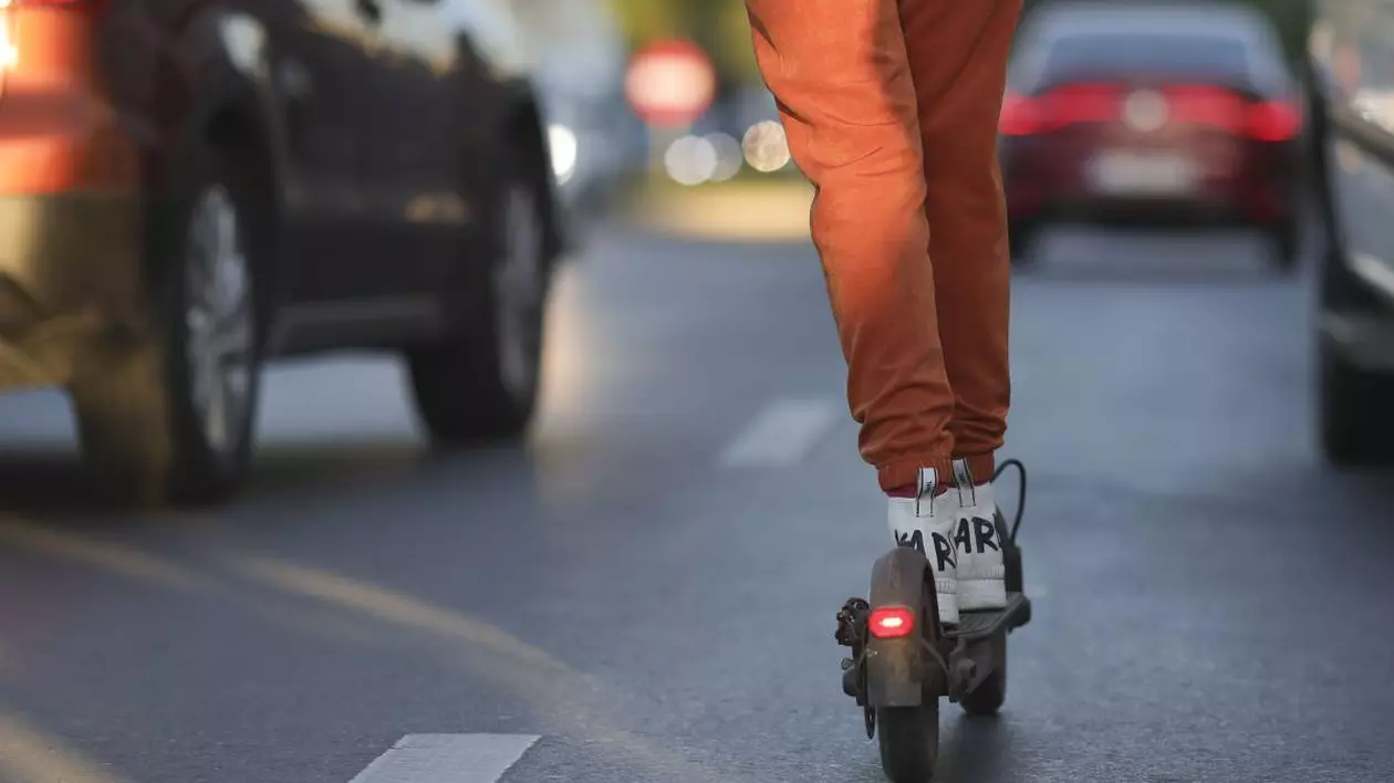 persoana imbracata cu pantaloni portocalii pe o trotineta electrica printre masini aflate in trafic