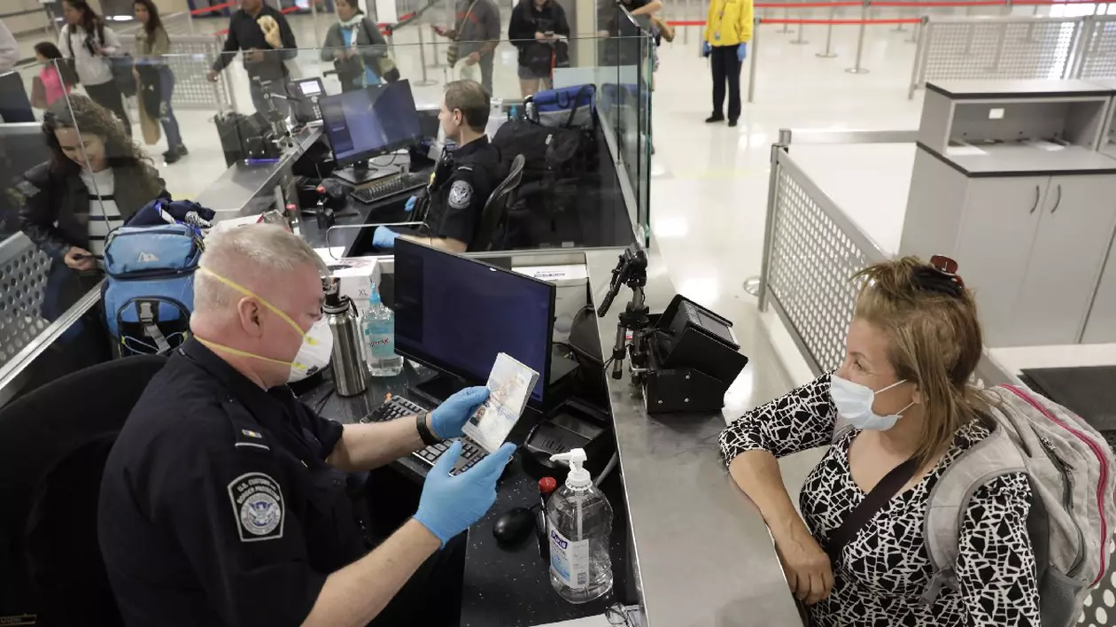 Ofițerii Serviciului Vamal și de Protecție a Frontierelor din SUA examinează pasagerii internaționali care sosesc la Aeroportul Internațional Dulles, purtând echipament de protecție personală, 13 martie 2020