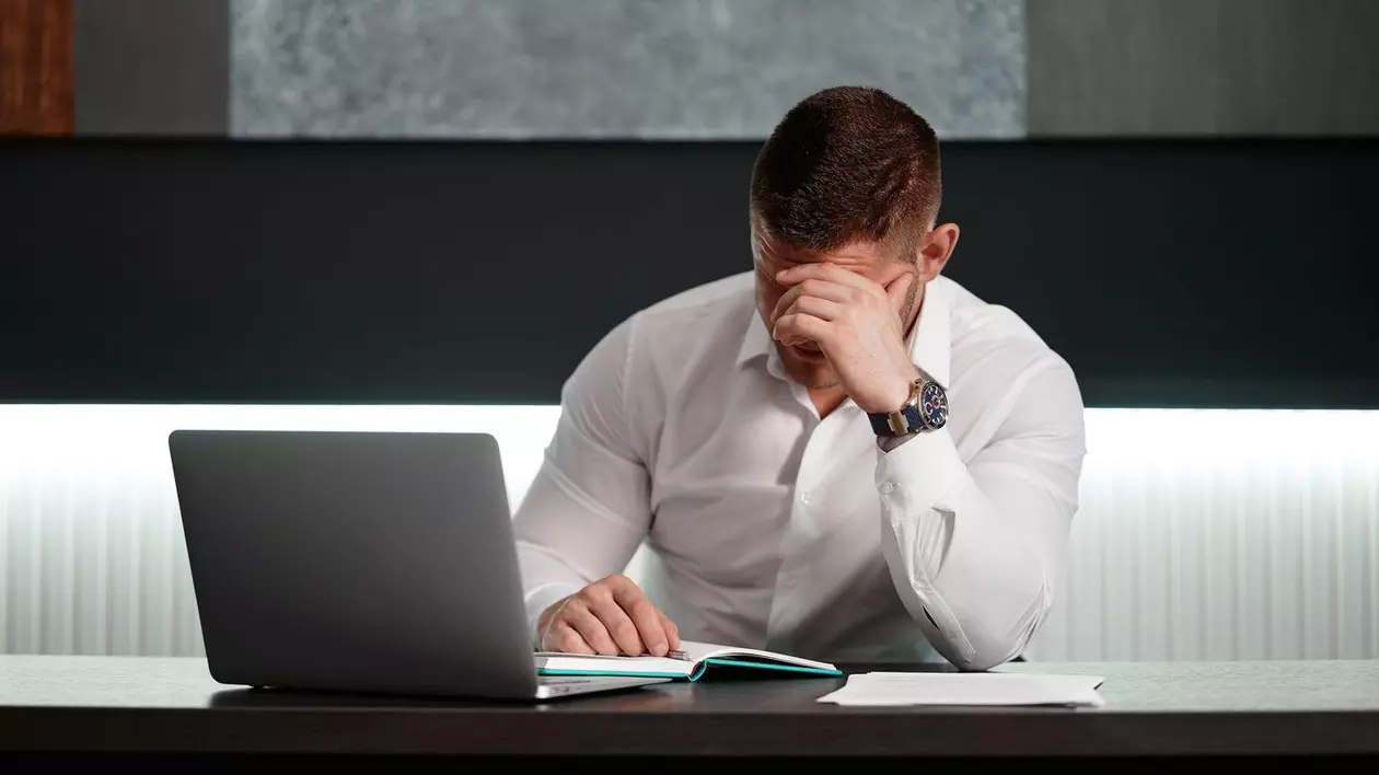 Bărbat în cămașă albă așezat la birou în fața calculatorului a coborât muntele cu mâna sub el