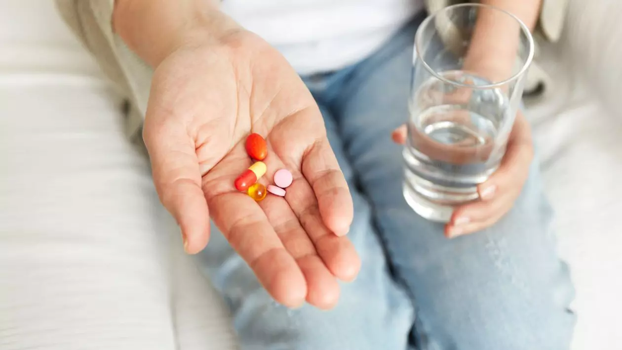 femeie care ține medicamente în palmă și un pahar de apă în mână