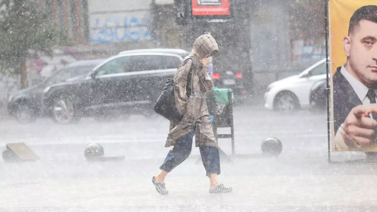 O femeie surprinsă de vremea rea în București merge pe stradă și trece pe lângă un afiș electoral. Foto: Libertatea/Dumitru Angelescu