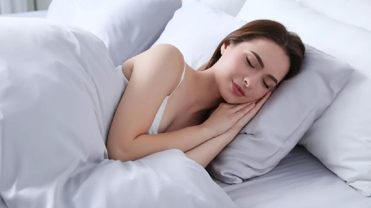 O tânără brunetă doarme într-un pat cu lenjerie de matase alba