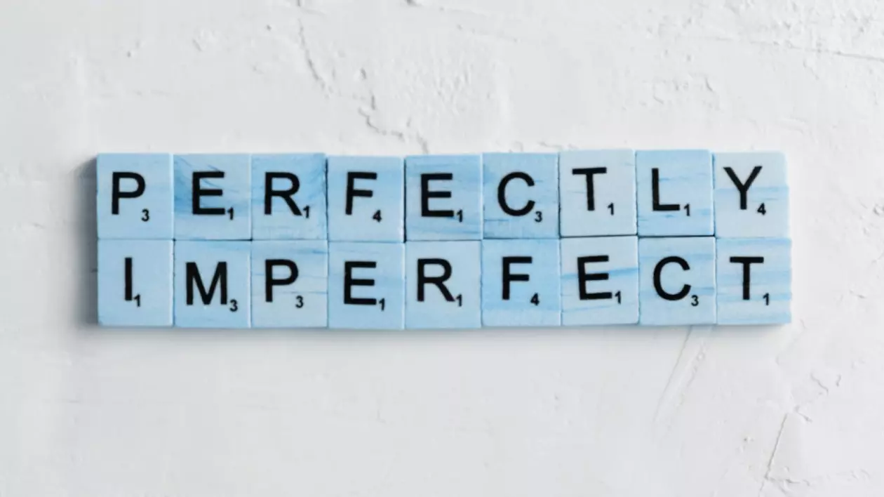 Fundal alb pe care sunt asezate cartonase de scrabble care formeaza cuvintele perfectly imperfect