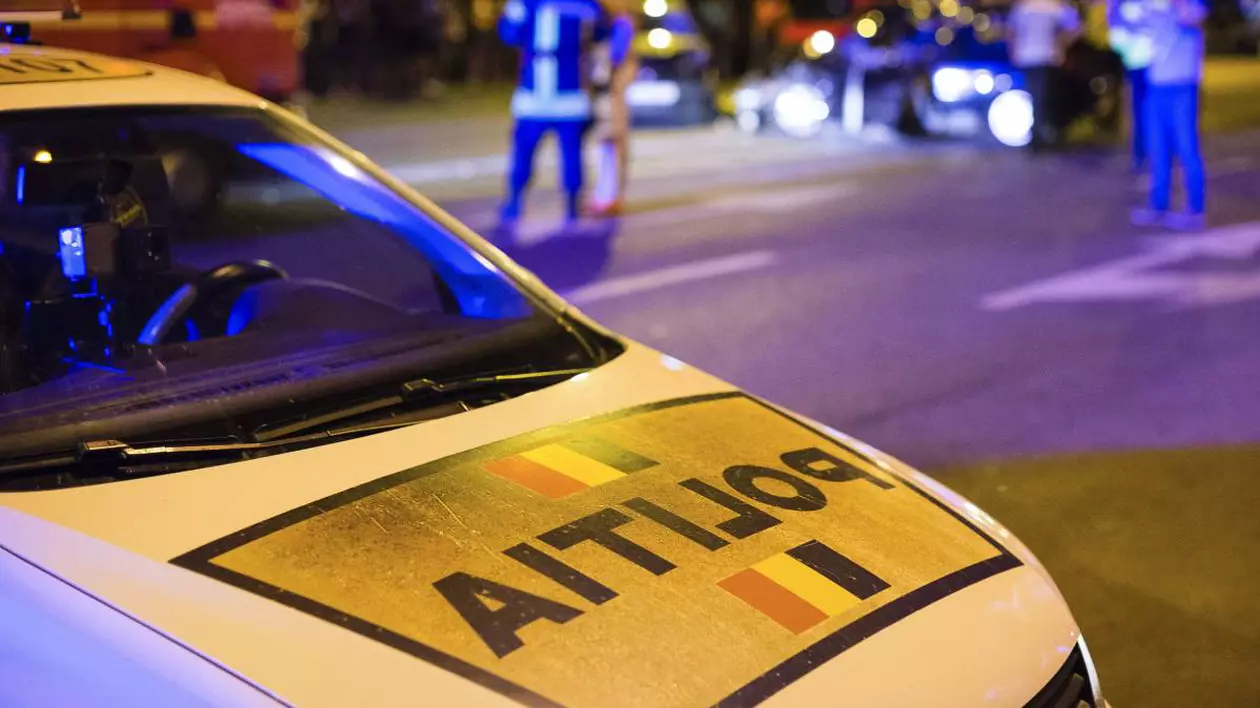 Fotografie în care în prim plan este o mașină a poliției, pe fundal agenți de poliție care fac măsurători în urma unui accident auto.