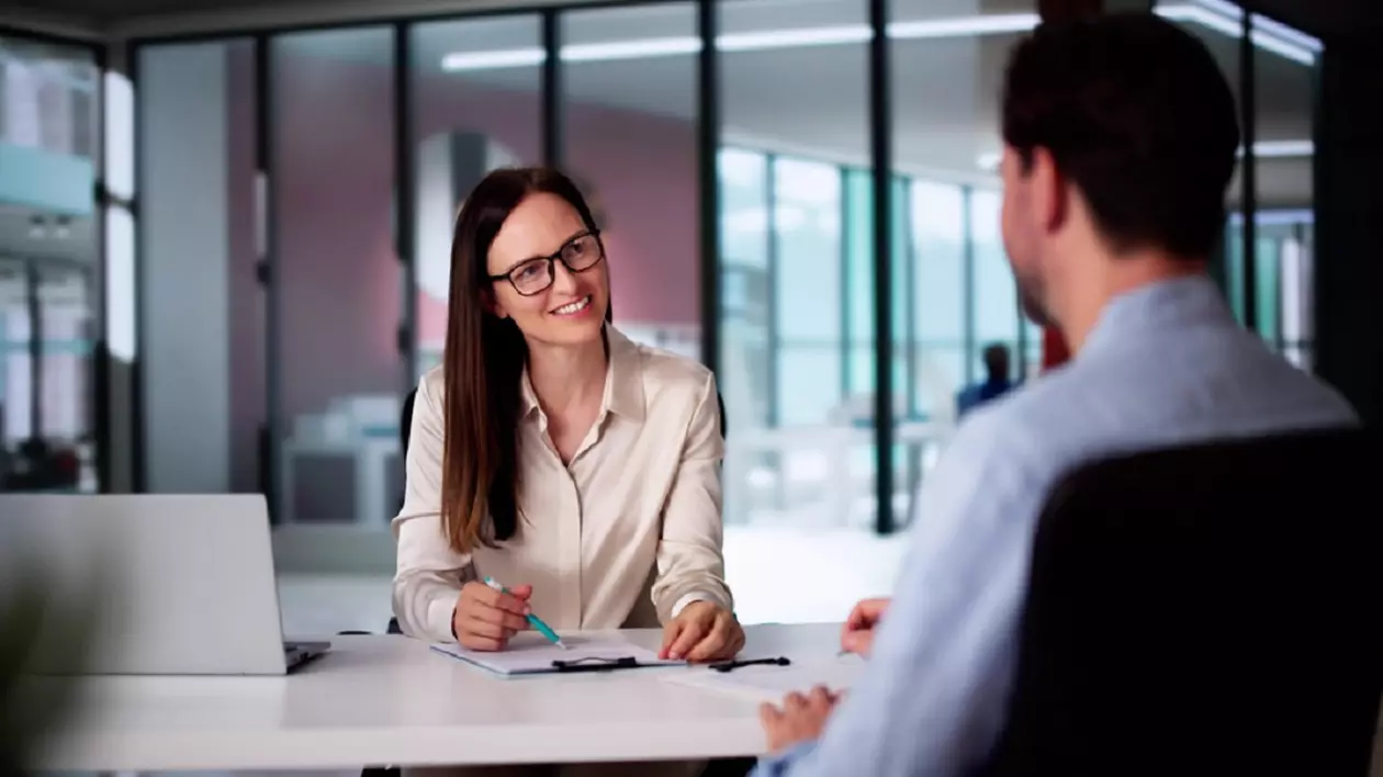 Un barbat, imbracat cu o camasa albastra, se afla la un interviu de job, cu o femeie de la HR, imbracata office cu o camasa alba