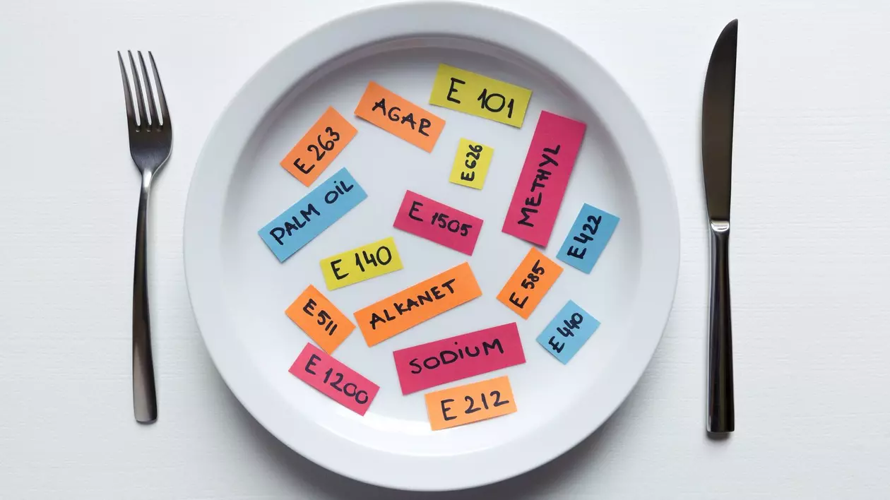 Farfurie albă cu notițe colorate pe care sunt notate aditivi alimentari. În dreapta este un cuțit, iar în stânga o furculiță