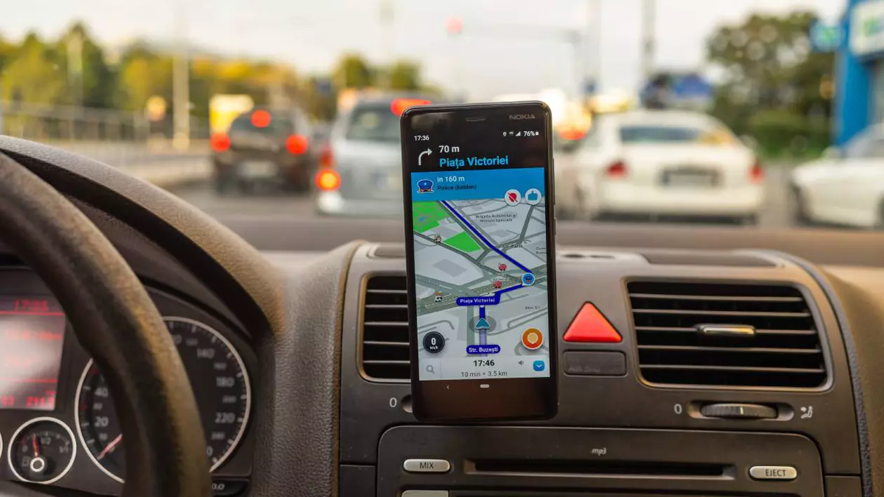 Interiorul unei mașini aflat în trafic, cu un telefon montat pe bord, afișând aplicația de navigație Waze.