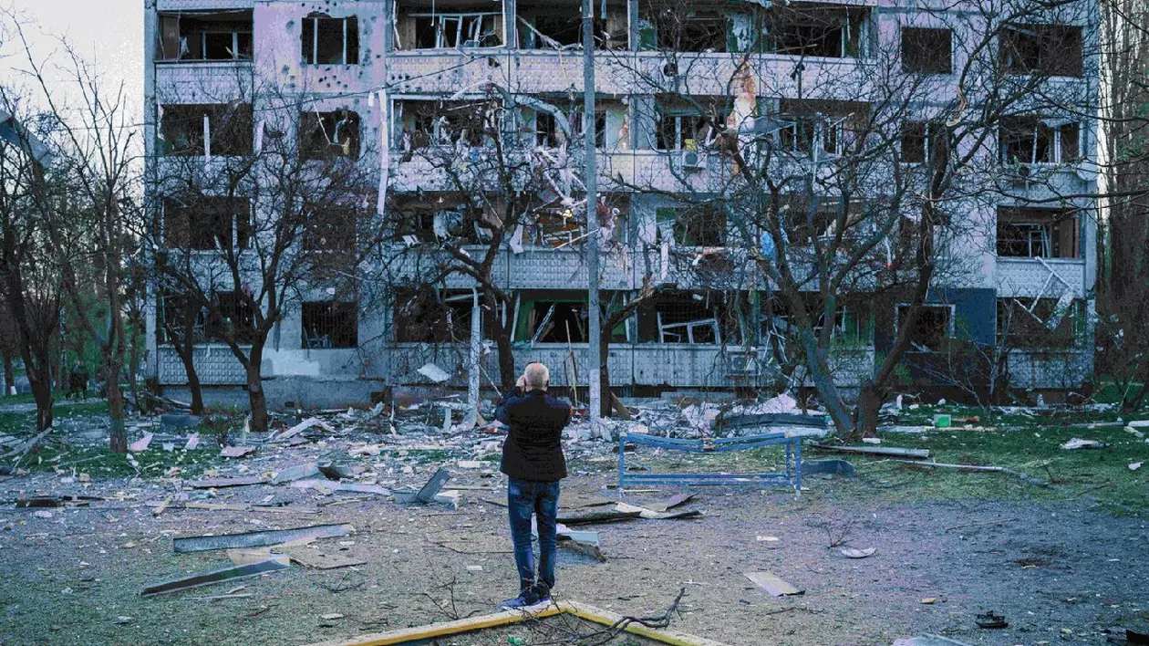 O vedere a unui bloc din Harkov după atacul Rusiei, un loc de joaca in fața căruia un bărbat ăncearca sa pozeze blocul devastat de explozie