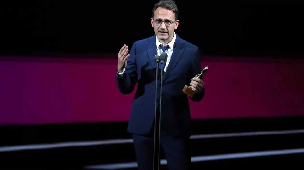 Bogdan Mureșanu surprins în timpul galei Premiilor Gopo vorbind la microfon și ținând în mâna dreaptă trofeul