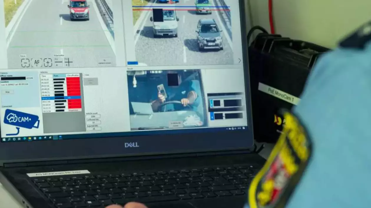 Un ofițer de poliție rutieră care urmărește pe ecranul unui laptop imagini surprinse de un sistem de monitorizare a traficului. Pe display se poate vedea clar cum un șofer ține telefonul mobil în mână în timp ce conduce, iar sistemul automat identifică vehiculul și salvează captura.