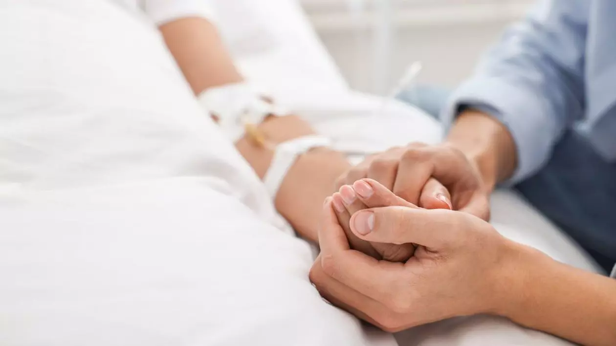 Un cadru medical ține de mână un bolnav aflat în spital, pe patul de moarte
