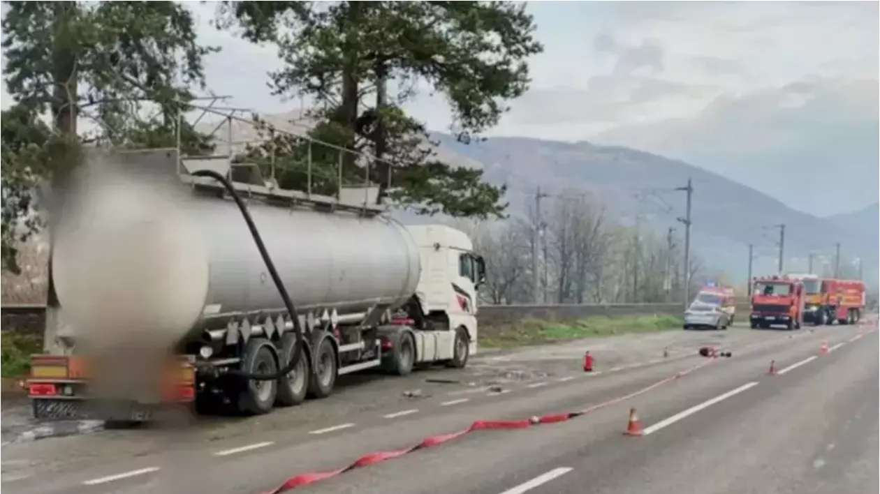 În imagine sunt ilustrate o cisternă, mașini de pompieri, o ambulanță, care sunt oprite pe marginea drumului.