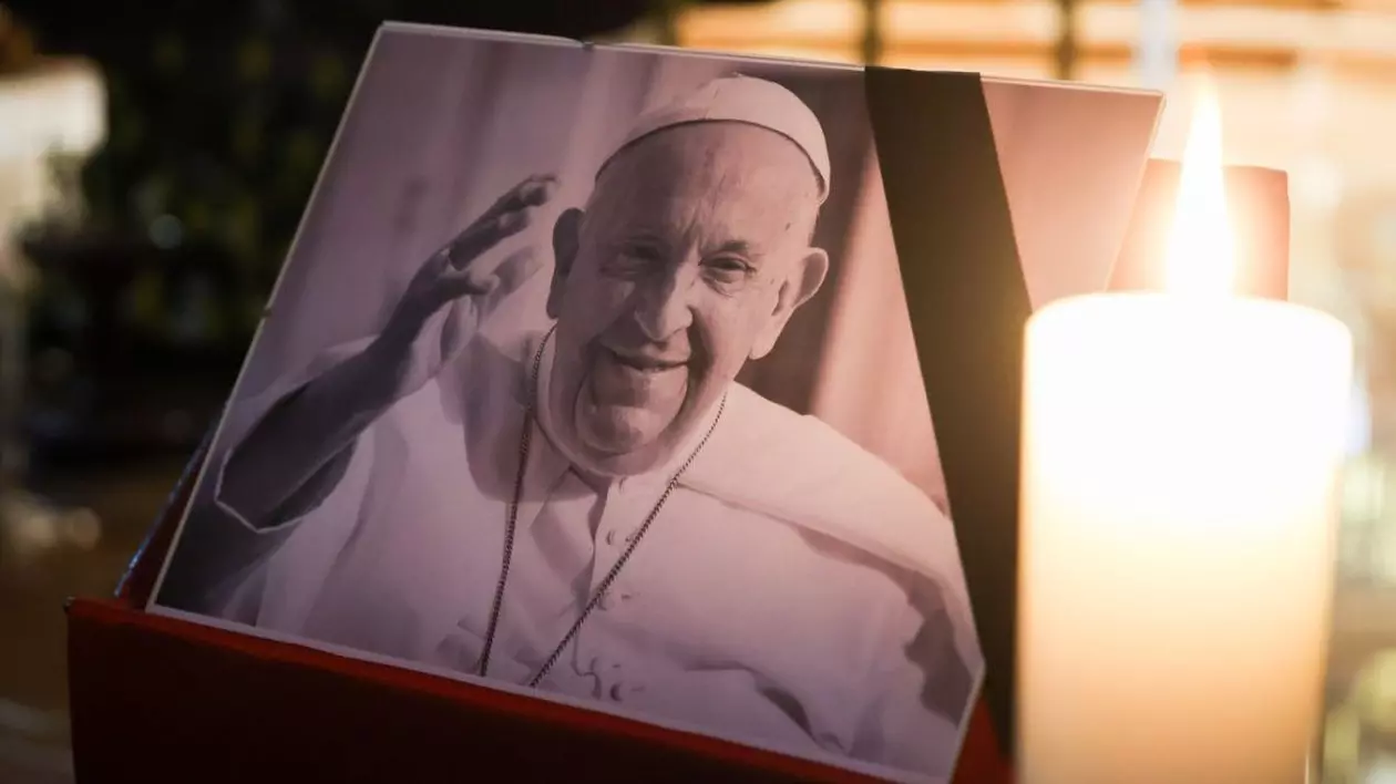 Papa Francisc a murit, fotografie alb negru cu Papa cu mâna ridicată, alături o lumânare care arde in prim-plan