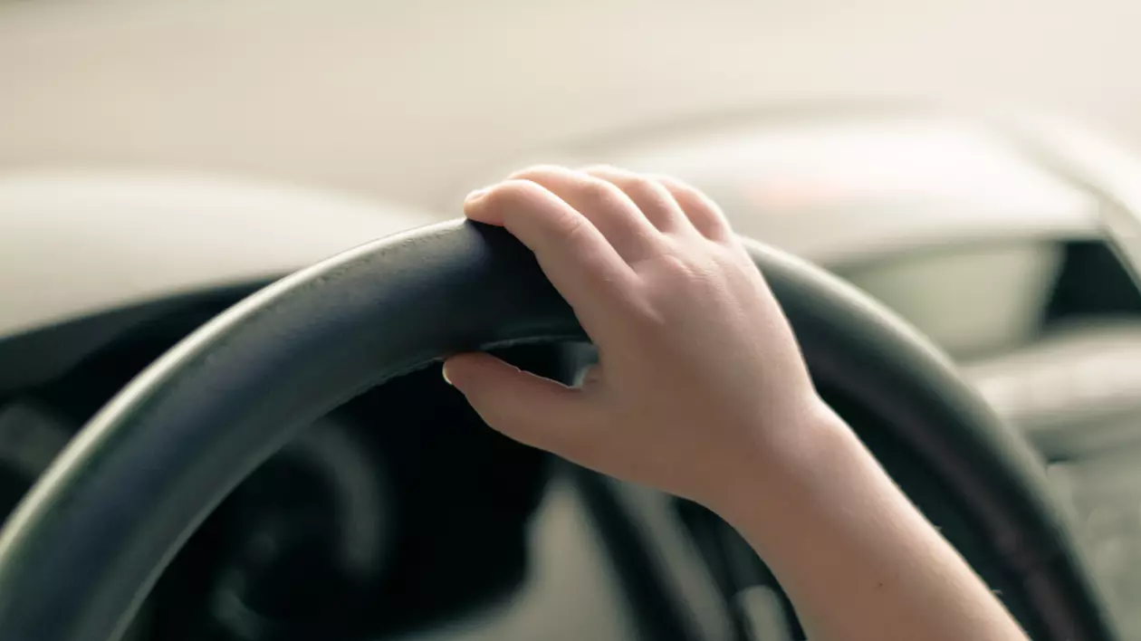 În imagine este ilustrată mâna unui copil pe volan