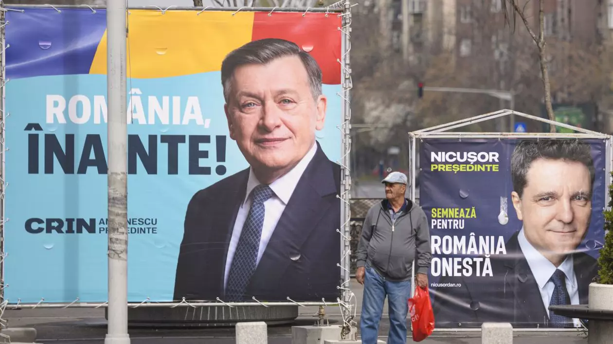 Bărbat surprins între două panouri electorale pe care apar Crin Antonescu și Nicușor Dan, candidați la alegerile prezidențiale din 4 mai 2025