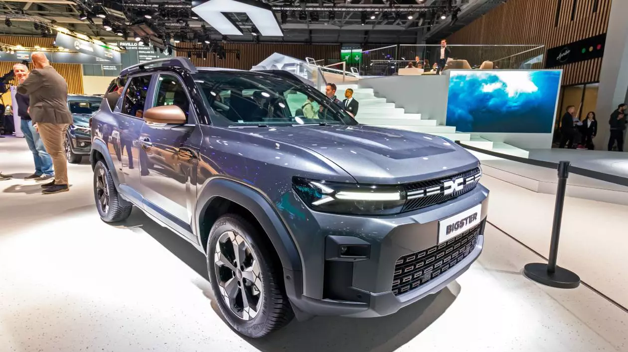Noul SUV Dacia Bigster expus într-un showroom auto, de culoare albastru inchis, pe fundal sunt cateva persoane care discută în jurul altor modele expuse