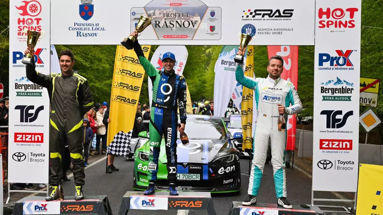 Podiumul competiției Trofeul Râșnov 2025. Pe locul 1 este Dominic Marcu, îmbrăcat în combinezon albastru, ținând trofeul ridicat, în fața unei mașini electrice Tesla Model S. Pe locurile 2 și 3 se află ceilalți doi concurenți de pe podium.