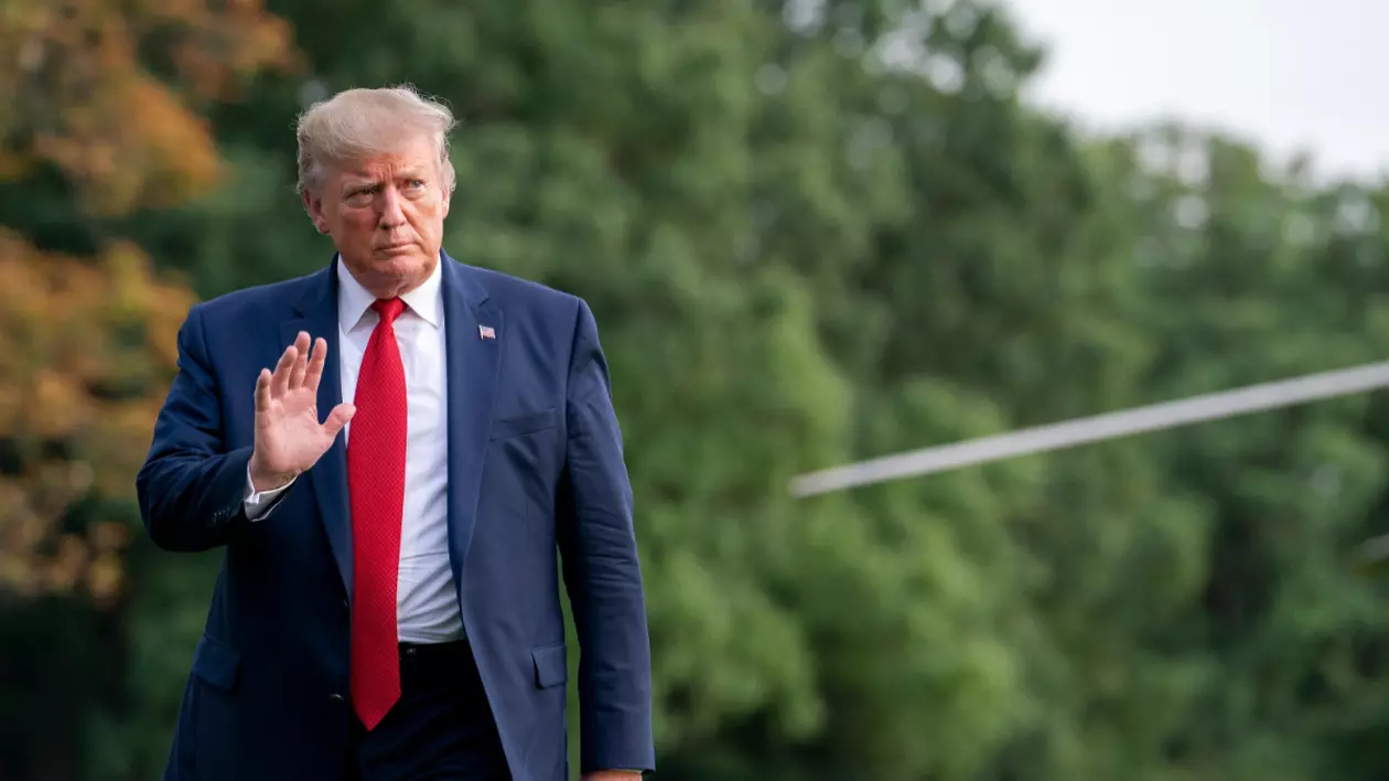 În imagine este ilustrat Donald Trump, care este îmbrăcat într-un costum albastru închis, poartă o cămașă albă și o cravată roșie