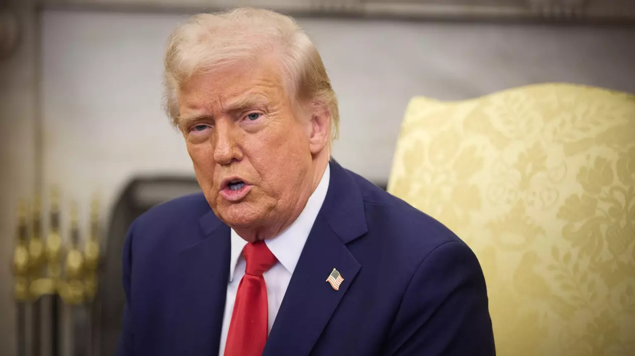 Președintele SUA Donald Trump stând pe scaun, purtând un sacou albastru, cu o cravată roșie și o cămașă albă
