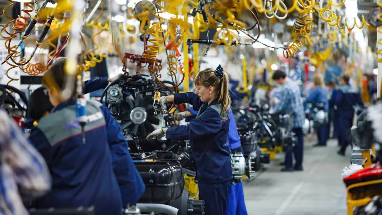muncitori imbracati in uniforma intr-o fabrica auto, se observa mai multe urilaje