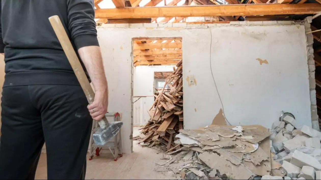 Un bărbat fotografiat cu spatele, îmbrăcat în negru, și cu un ciocan în mână este într-o casă în care e demolată o parte din ea