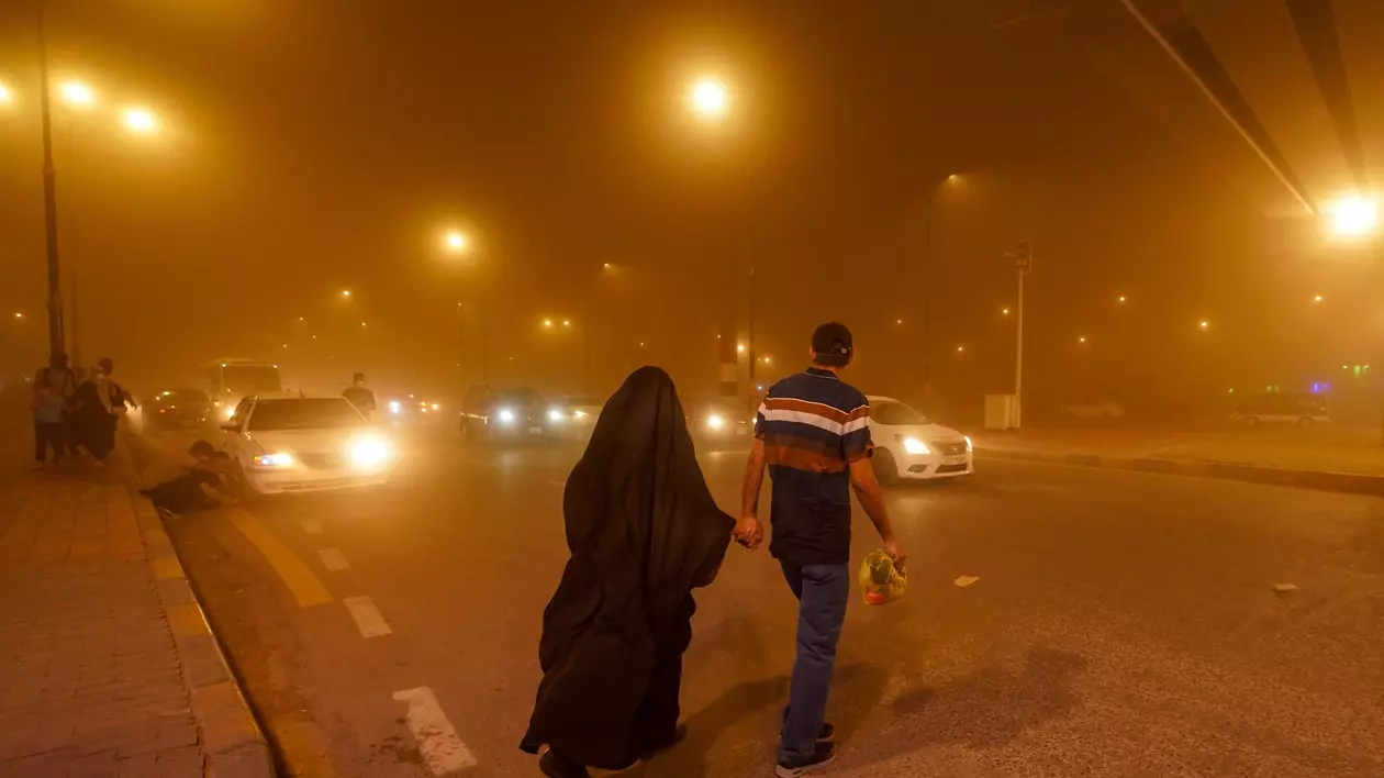 un bărbat ține o femeie de mână și aversează strada în Irak, în timpul unei furtuni de nisip