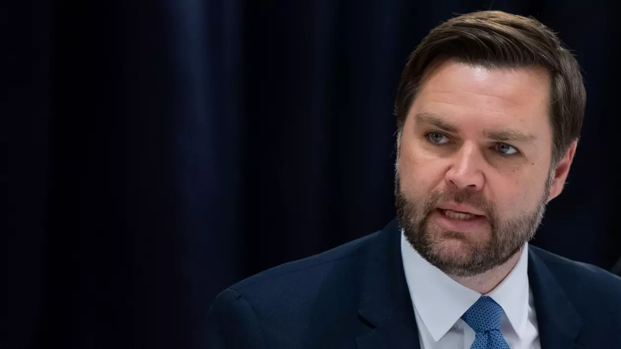 JD Vance surprins în timp ce vorbește. Poartă un sacou negru, o cămașă albă și o cravată albastră.