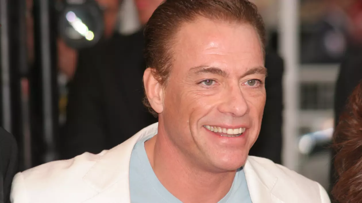 În imagine este ilustrat Jean Claude Van Damme, în sacou alb și tricou turcoaz
