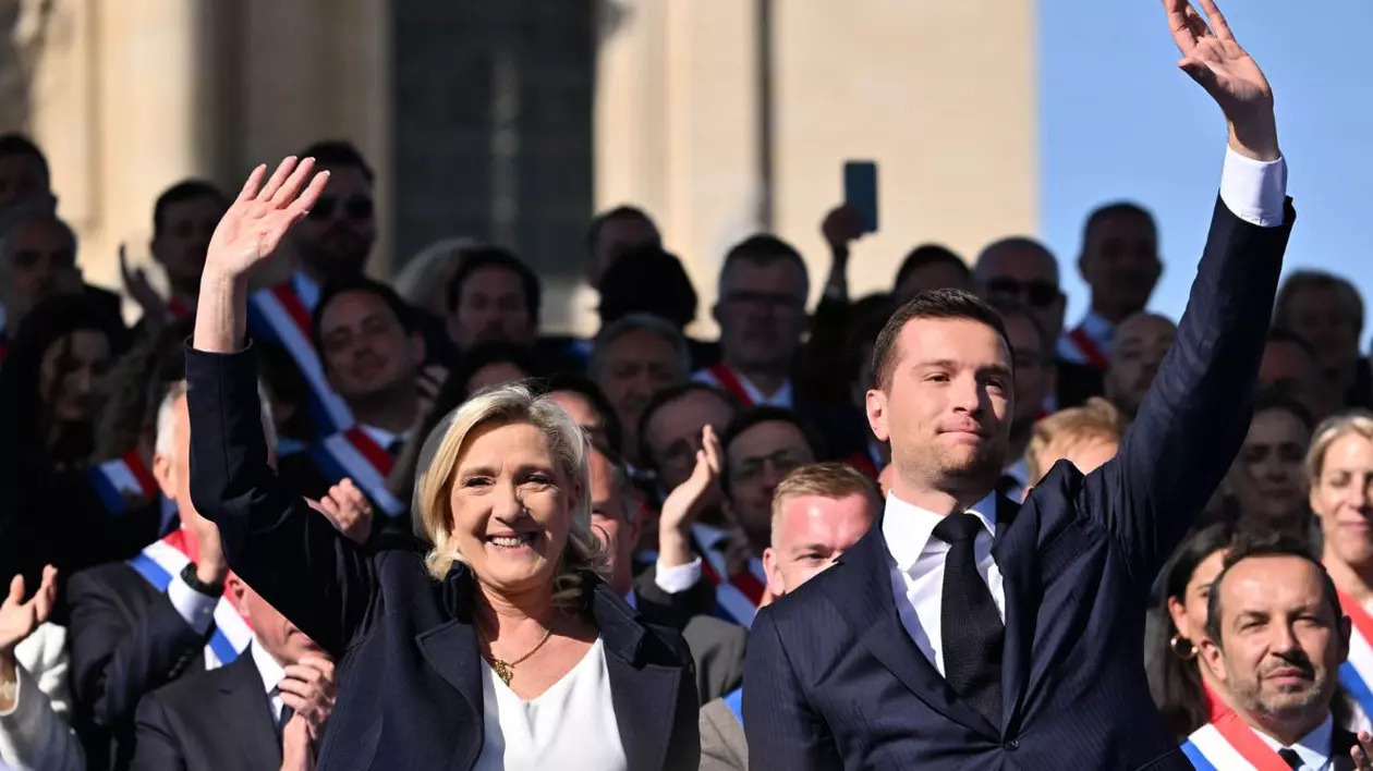 Jordan Bardella și Marine le Pen, ridicând mâna în aer, îmbrăcați în costume negre cu cămăși albe