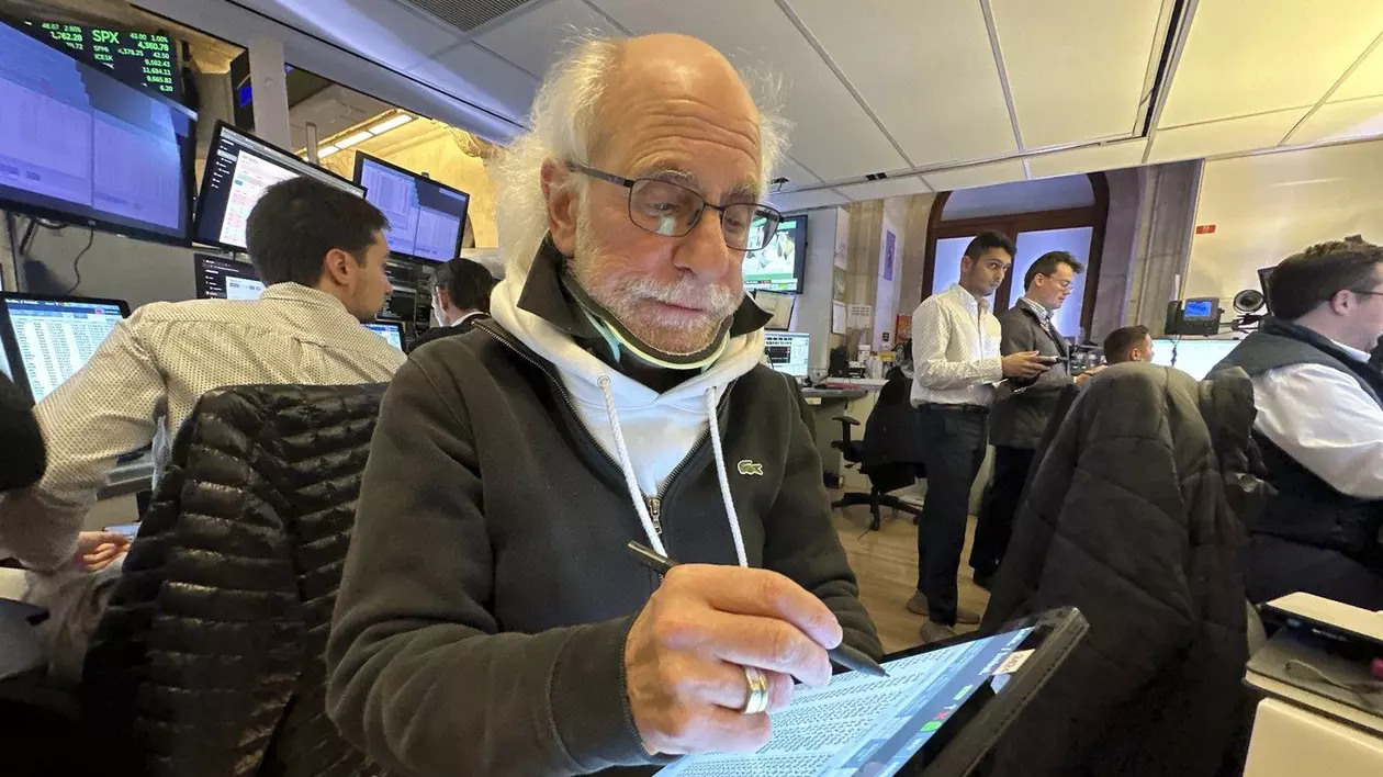 Peter Tuchman, legendarul trader de pe bursa din New York, notează într-un caiet. In plan departat se pot vedea alti lucratori la bursa americana si ecrane cu indici bursieri
