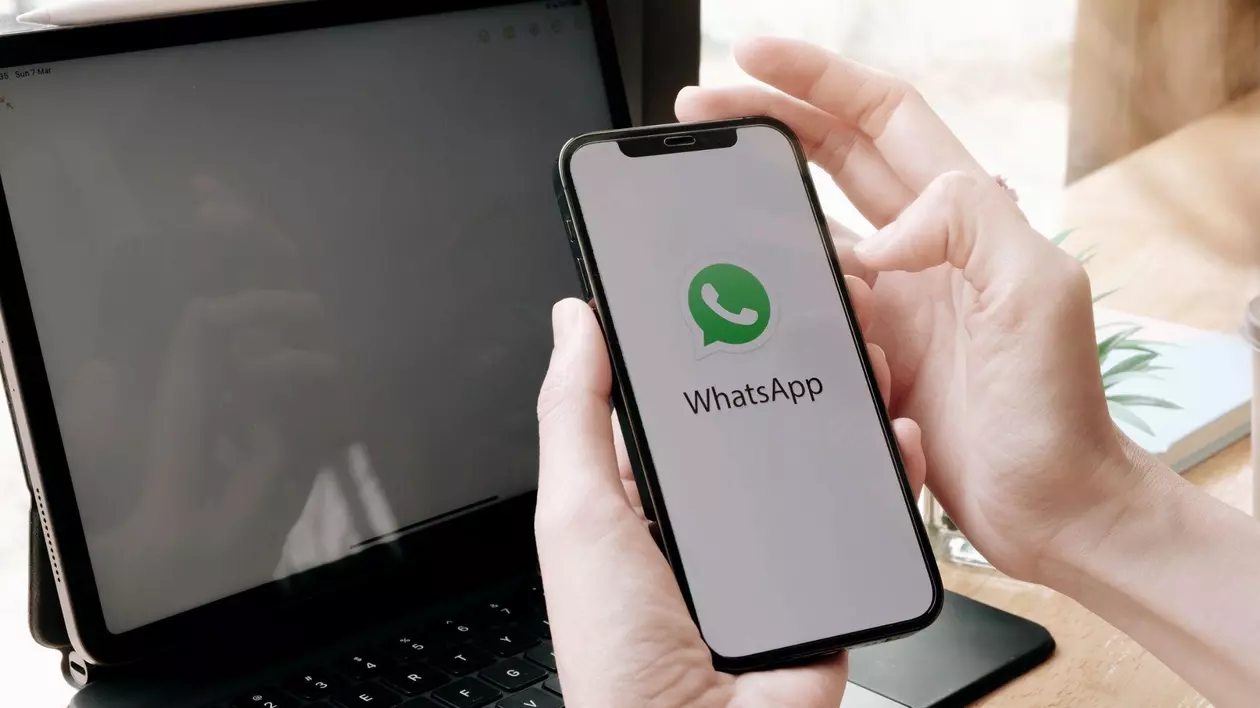 Maine de barbat care tin un telefon deschis pe Whatsapp in fata unei laptop