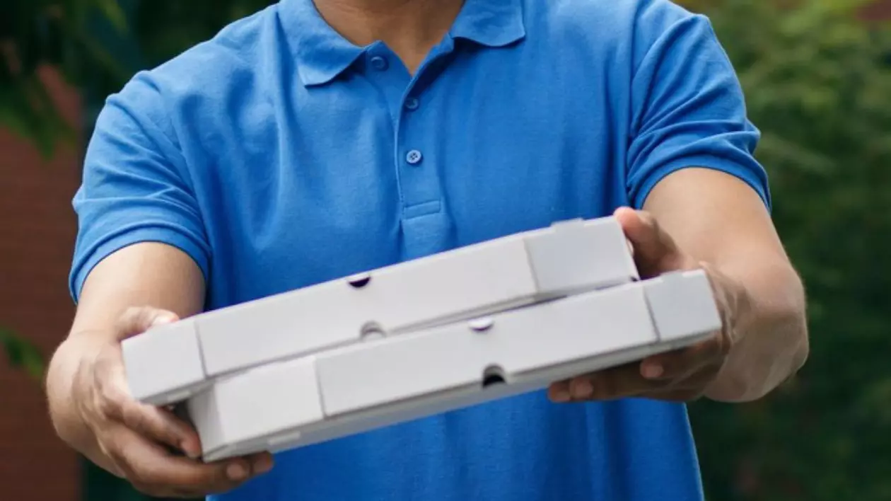 Bustul unui bărbat cu un tricou albastru cu mâinile întinse care tin doua cutii de pizza