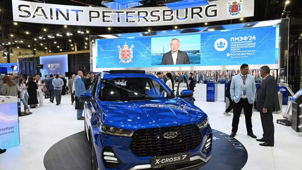 Showroom auto de la Sankt Petersburg. În prim-plan este expus un SUV albastru model X-Cross 7. În fundal, un ecran mare, iar în jurul mașinii câteva persoane care discută posibil despre modelul auto expus.