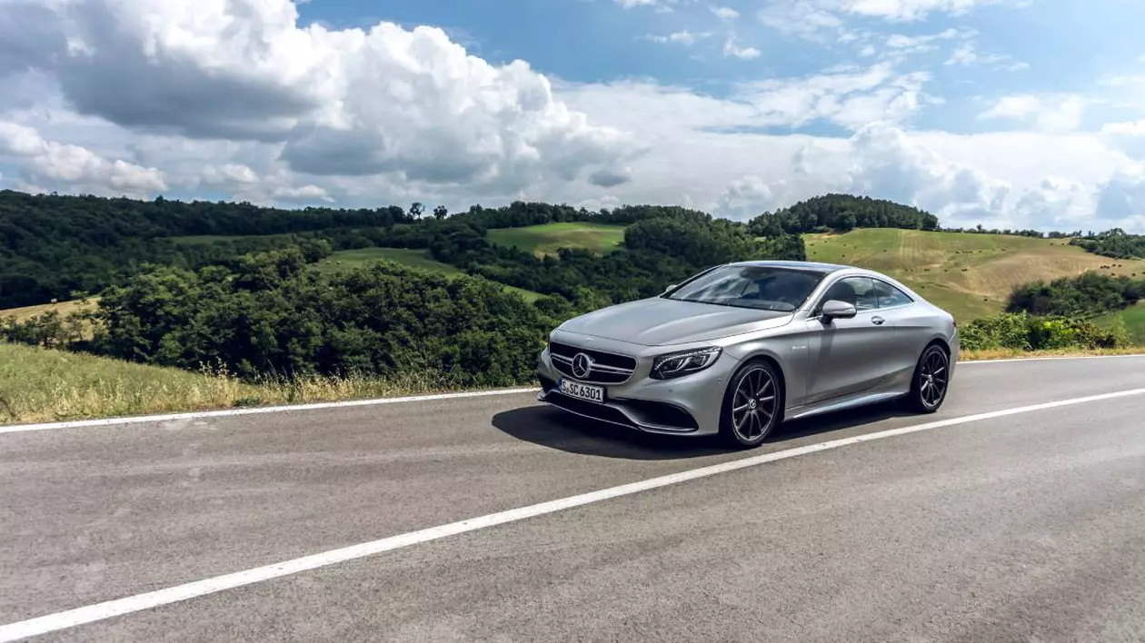 Mercedes-Benz sport-coupe, de culoare gri metalizat, condus pe un drum cu dealuri verzi