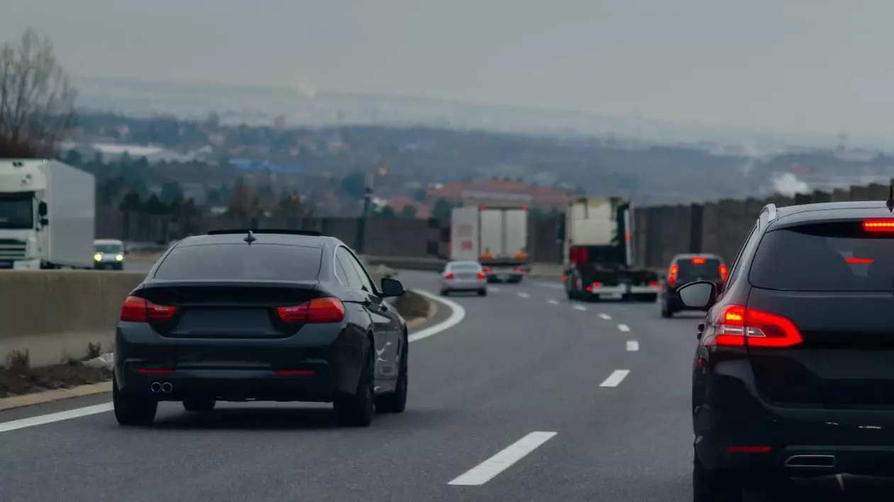 Autotradă aglomerată cu două benzi pe sens desparțite de un parapet.În prim plan sunt doua mașini negre, una care circulă pe banda doi, iar cealaltă pe banda unu.