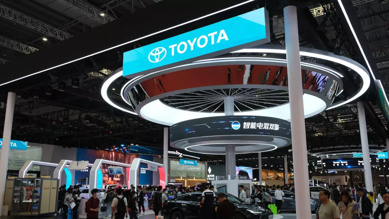 Stand al companiei Toyota la un târg internațional auto din China cu ecrane LED care afișează logo-ul Toyota și mesaje în limba chineză. În mijlocul standului se află o mașină neagră de prezentare