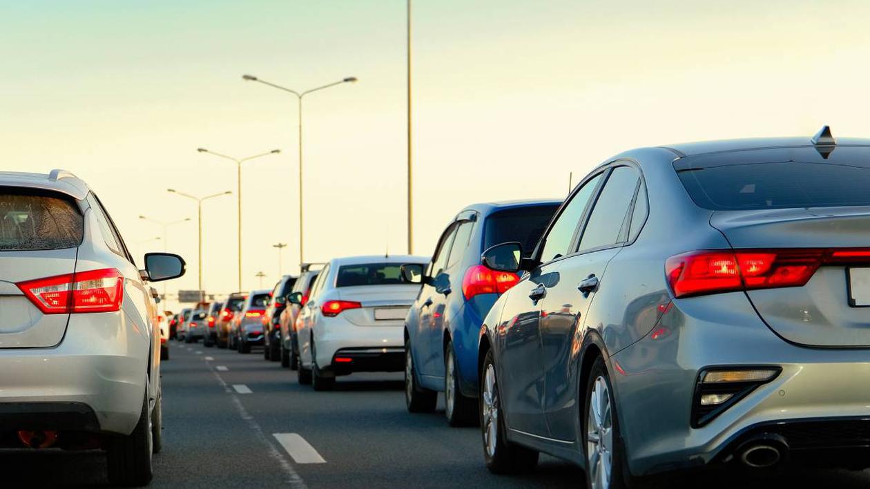 Mai multe mașini aflate în linie, pe un drum cu două benzi pe sens, posibil o autostradă.
