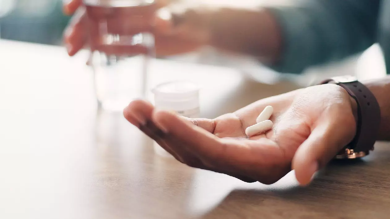 Un om care tine în palmă doua medicamente si un pahar cu apa