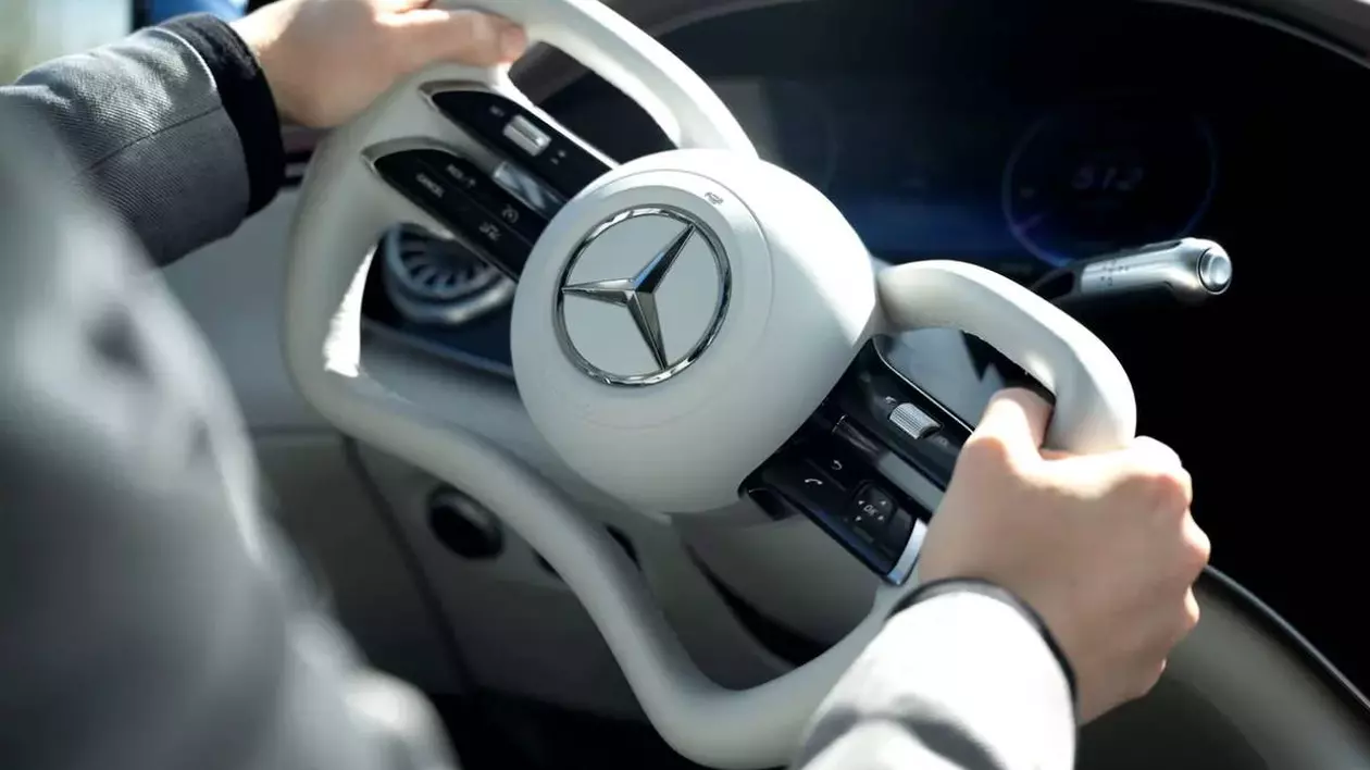 Interiorul unei mașini Mercedes Benz, în prim plan este noul design al volanului, asemanator cu manșa unui avion. se observă sigla mercedes de culoare argitie, iar volanul este de culoare alba dintr-un material de piele