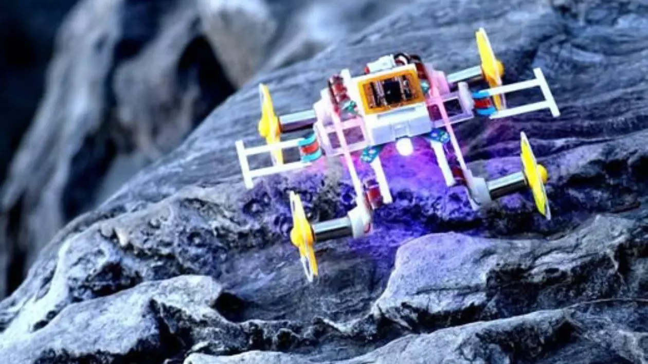 Un micro-robot care se aseamănă unei piese Lego, pe un fundal de rocă gri-albastră.