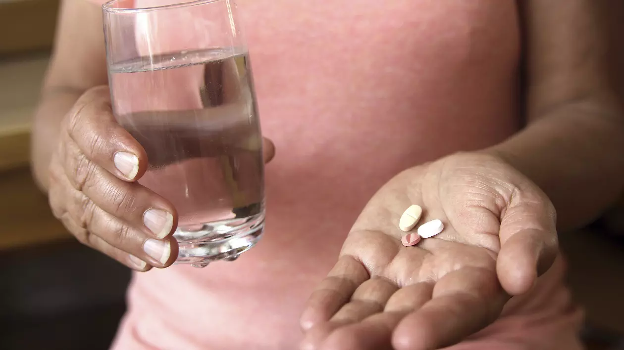 o femeie cu un pahar de apa și trei medicamente