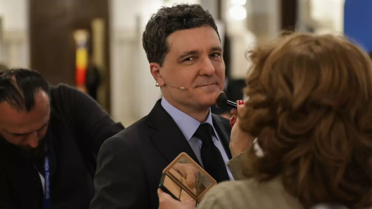 Nicușor Dan așteaptă să fie machiat pentru dezbatere. O femeie îi trece o pensulă de întins fondul de ten pe față