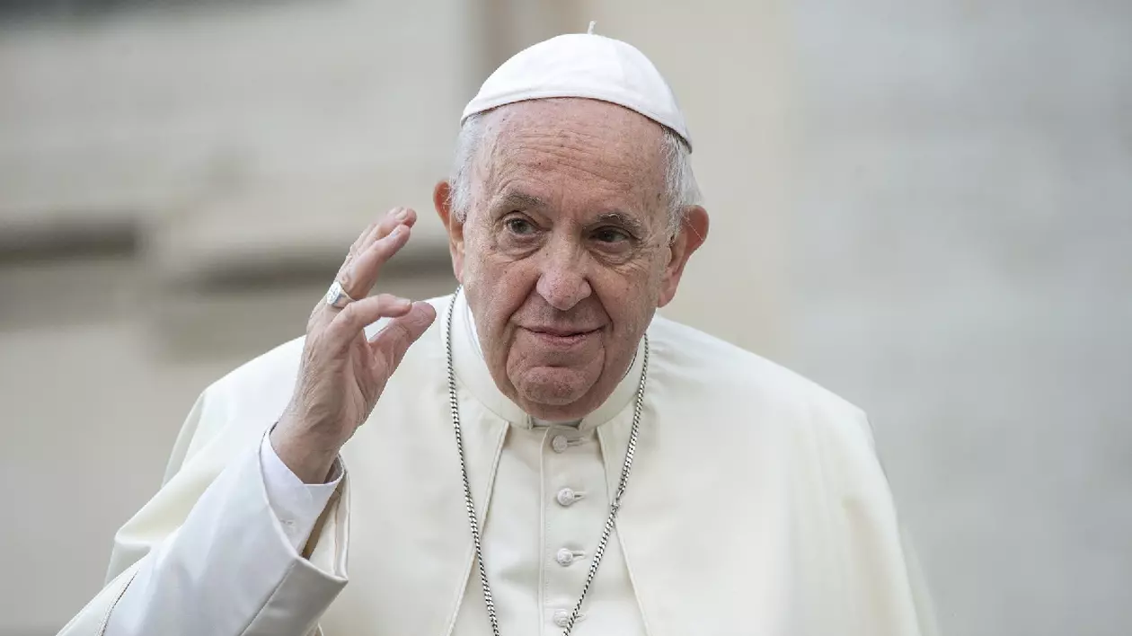 În imagine este ilustrat Papa Francisc, în timp ce ține mâna dreaptă ridicată