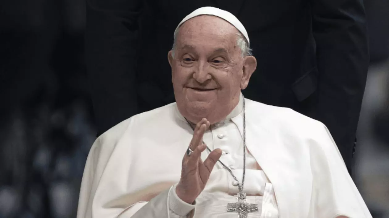 În imagine este ilustrat Papa Francisc, în timp ce ține mâna dreaptă ridicată
