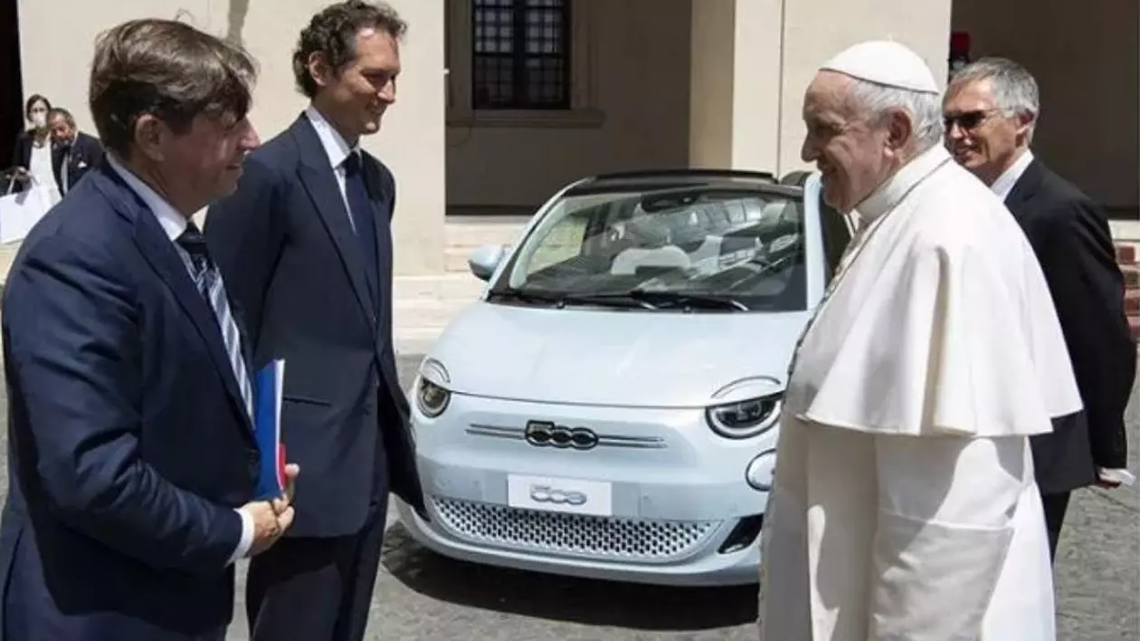 Papa Francisc îmbrăcat cu tradiționala vestimentație albă, în timpul unei discuții cu mai mulți oficiali, în fața unei mașini electrice Fiat 500 de culoare albă.