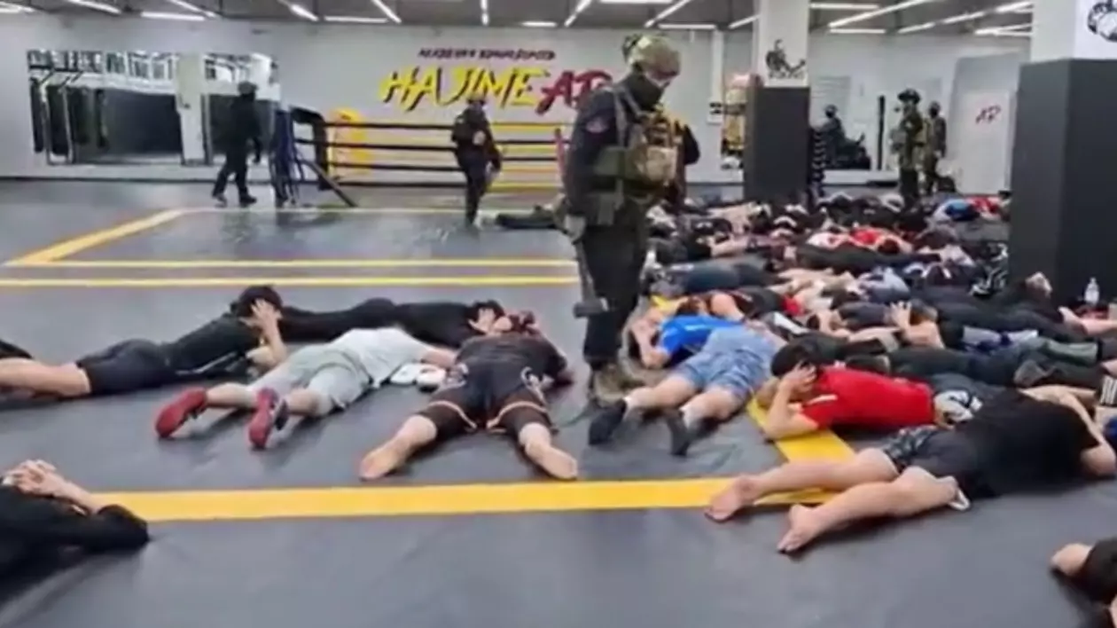 În imagine sunt ilustrați oameni întinși pe jos, în sala de sport, și polițiști care au intrat peste ei