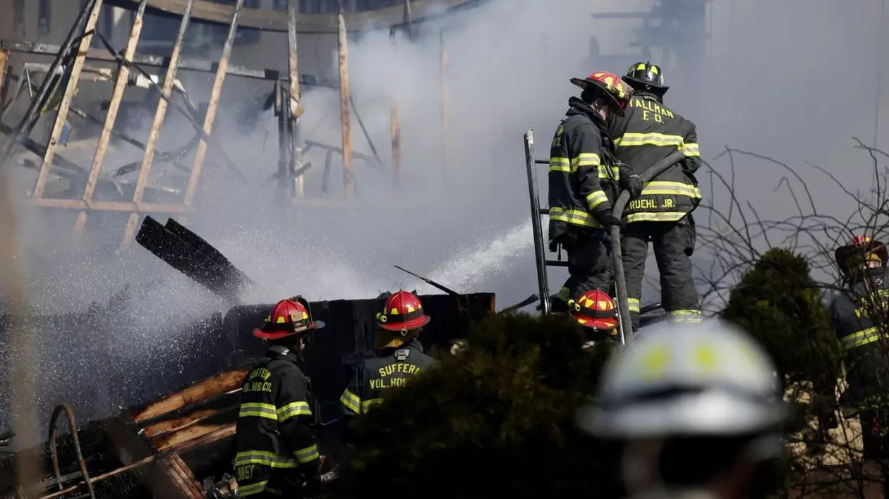 Pompierii continuă să dea în zonele în care încă arde cu apă de la un furtun de incendiu, după ce un foc a izbucnit la Evergreen Court Home for Adults din Spring Valley, New York, 23 martie 2021