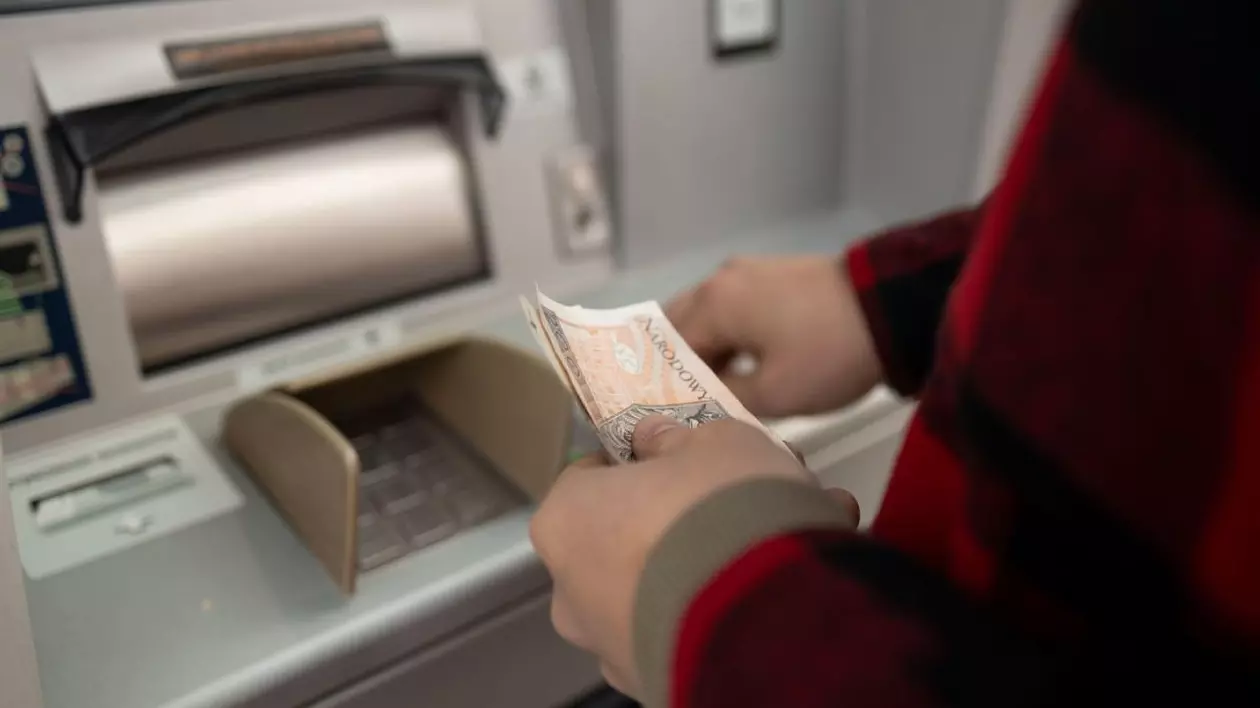 Prim-plan al unui bărbat care ia bani de la un bancomat, retrage numerar