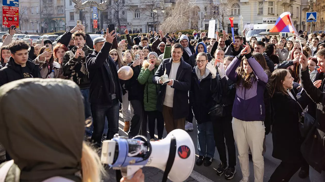 Protest studenți Novi Sad. In imagine se vede o multime de studenti care protesteaza, ia rin fata lor o persoana cu portavoce care pare sa dea tonul scandarilor