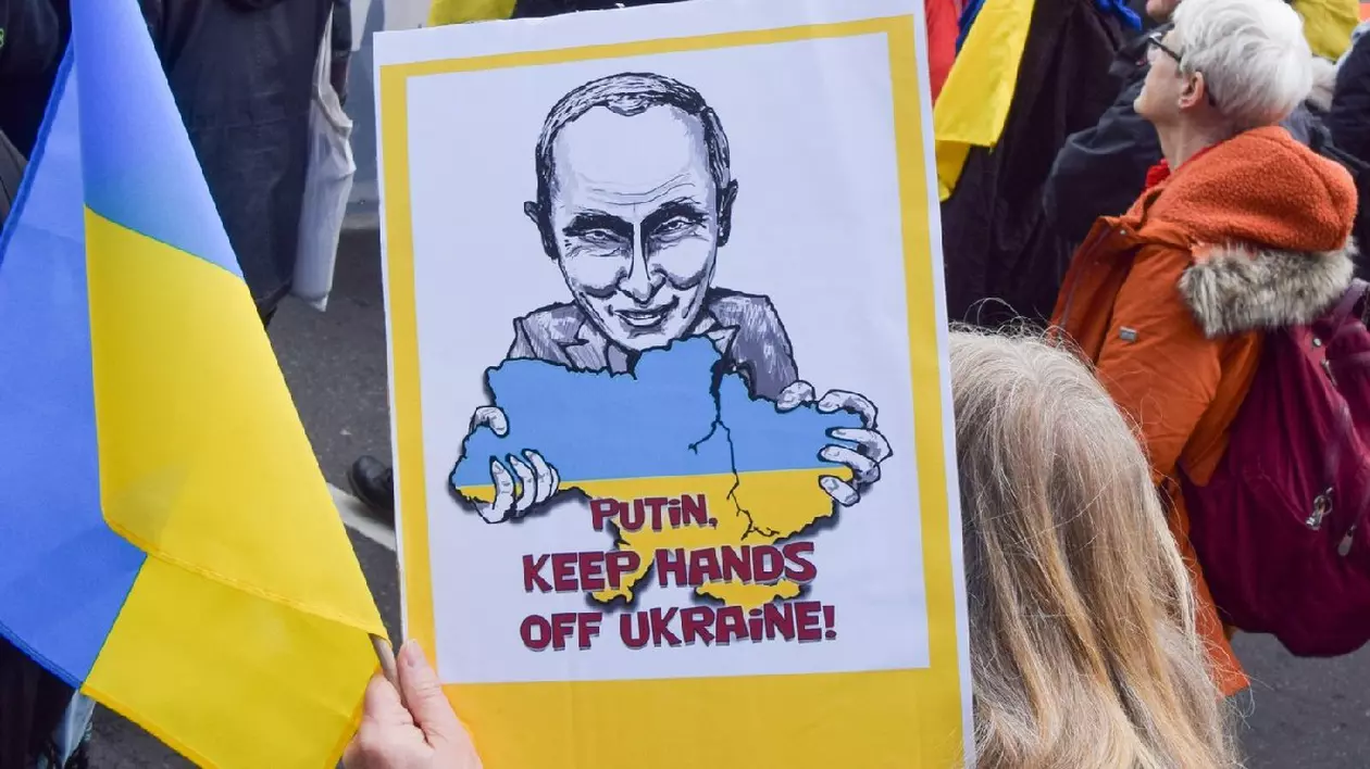 Oameni prezenti la un protest în Londra, mărșăluiesc spre Ambasada Rusiei în semn de solidaritate cu Ucraina, înaintea celei de-a treia aniversări a atacului Rusiei. Afis cu Vladimir Putin care ține în mâini harta Ucrainei, unde scrie Putin, jos mâinile de pe Ucraina